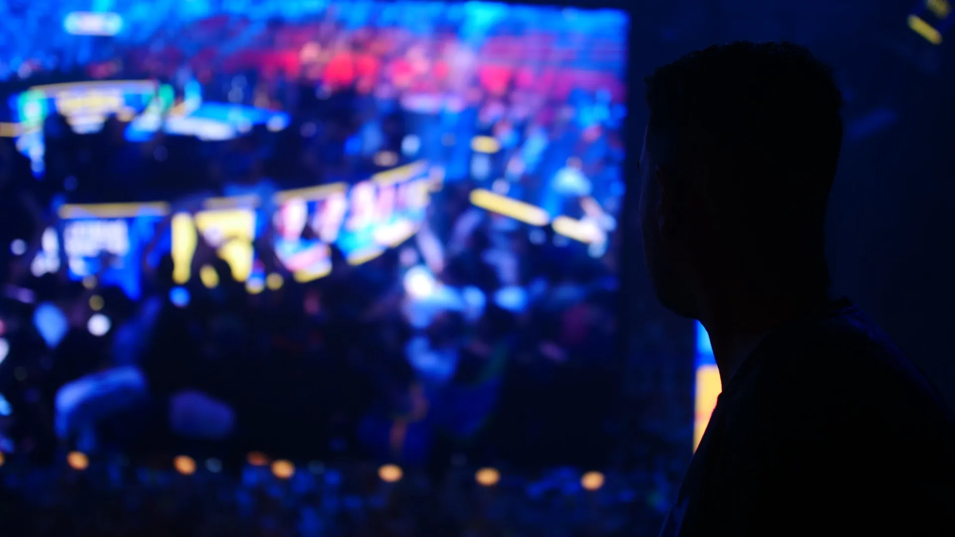 One person in silhouette facing a blurred arena under stage lights.